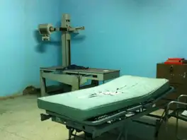 Hospital X-ray room with a broken drop ceiling and a gurney with a torn mattress.