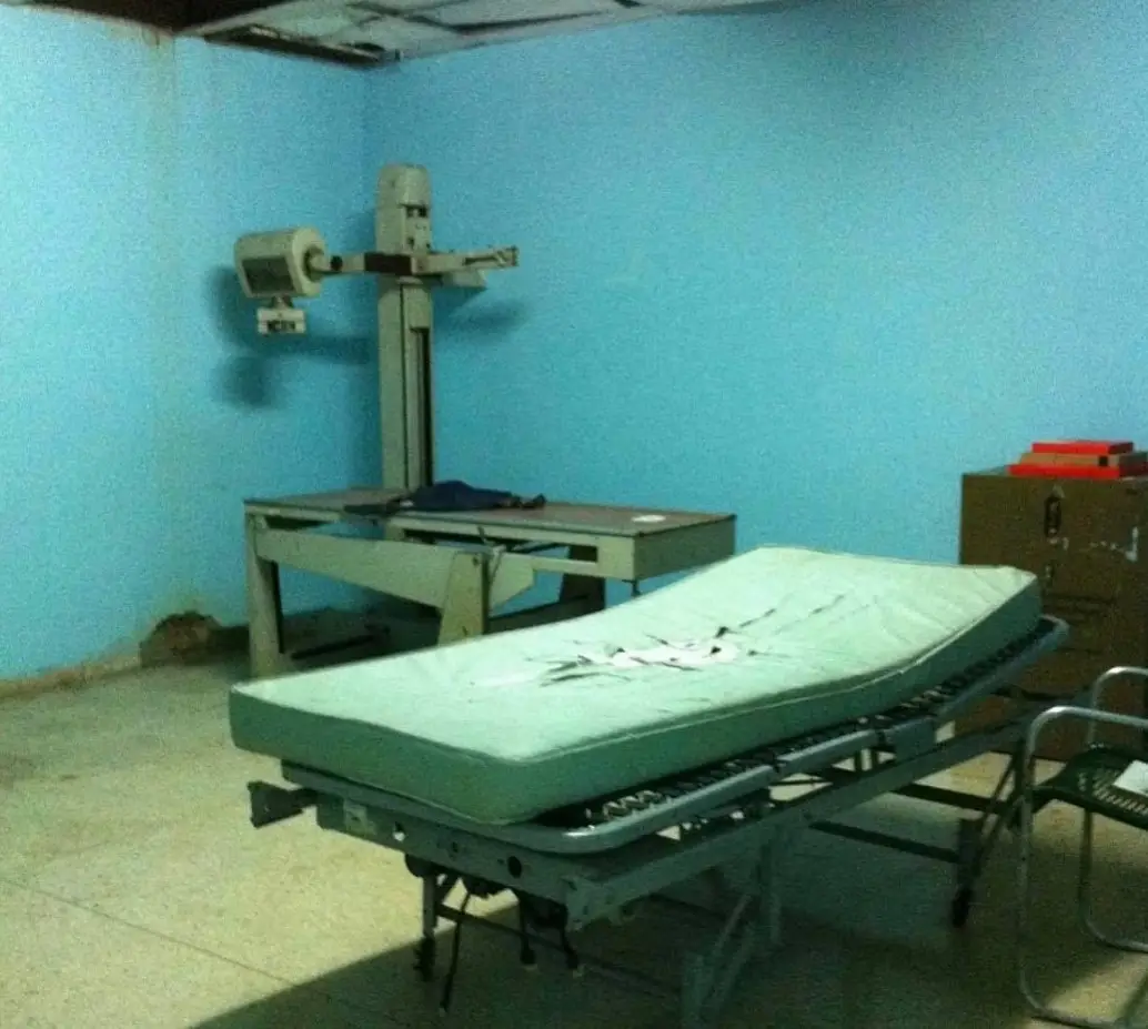 Hospital X-ray room with a broken drop ceiling and a gurney with a torn mattress.