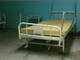 Hospital bed with a bare foam mattress and wooden slats tied to the rails.