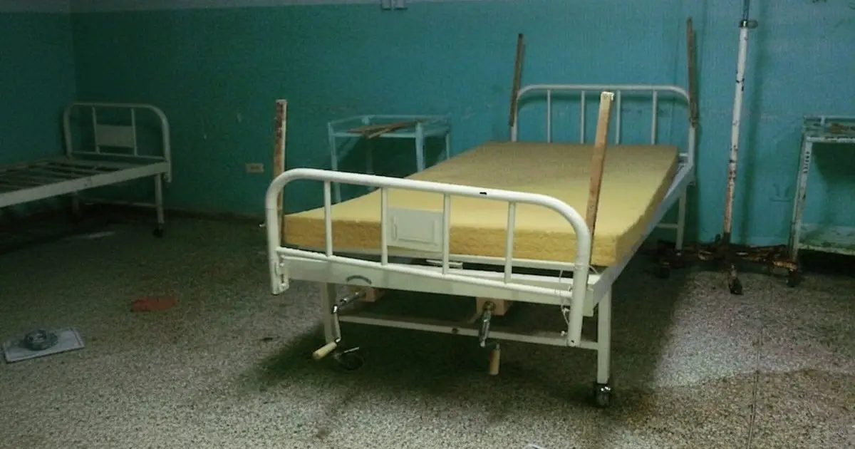 Hospital bed with a bare foam mattress and wooden slats tied to the rails.